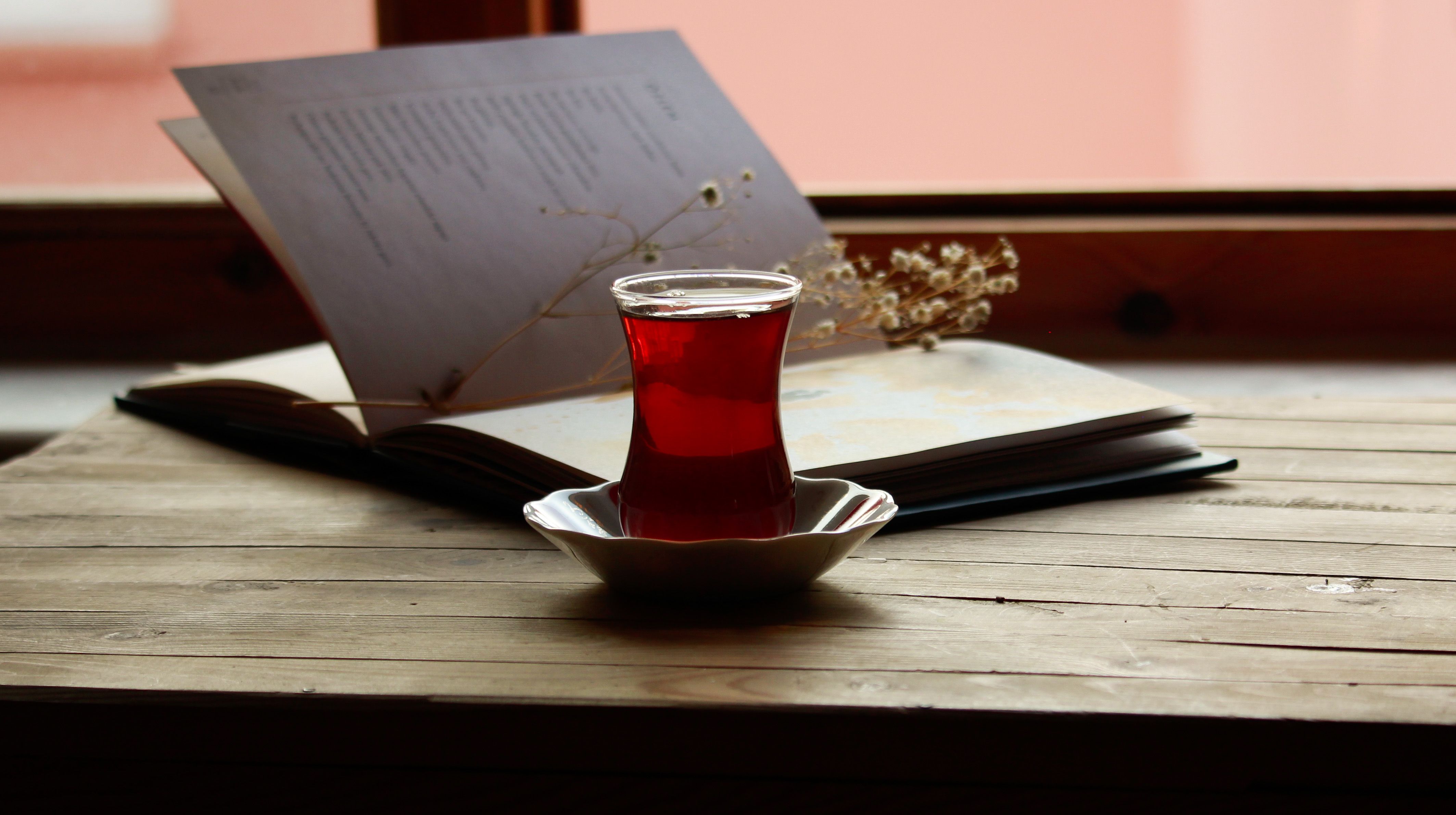 An open book and a glass of tea on a wooden table by a window