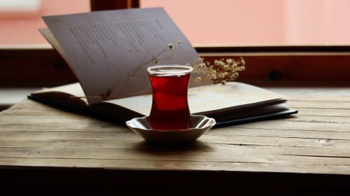 Free A peaceful setting featuring a glass of tea and an open book on a wooden table by the window. Stock Photo