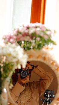 Woman using DSLR camera in mirror reflection surrounded by flowers.