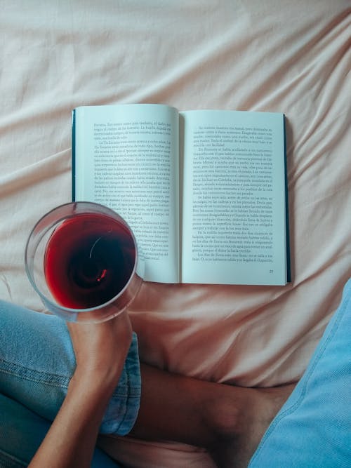 Free A Person Holding a Glass of Wine over a Book Stock Photo