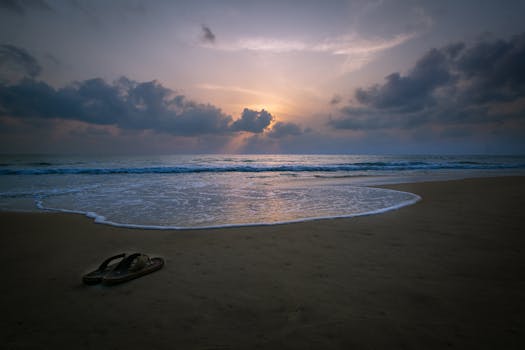 Dramatic sunset over a quiet beach with waves and slippers in the sand, creating a serene atmosphere.