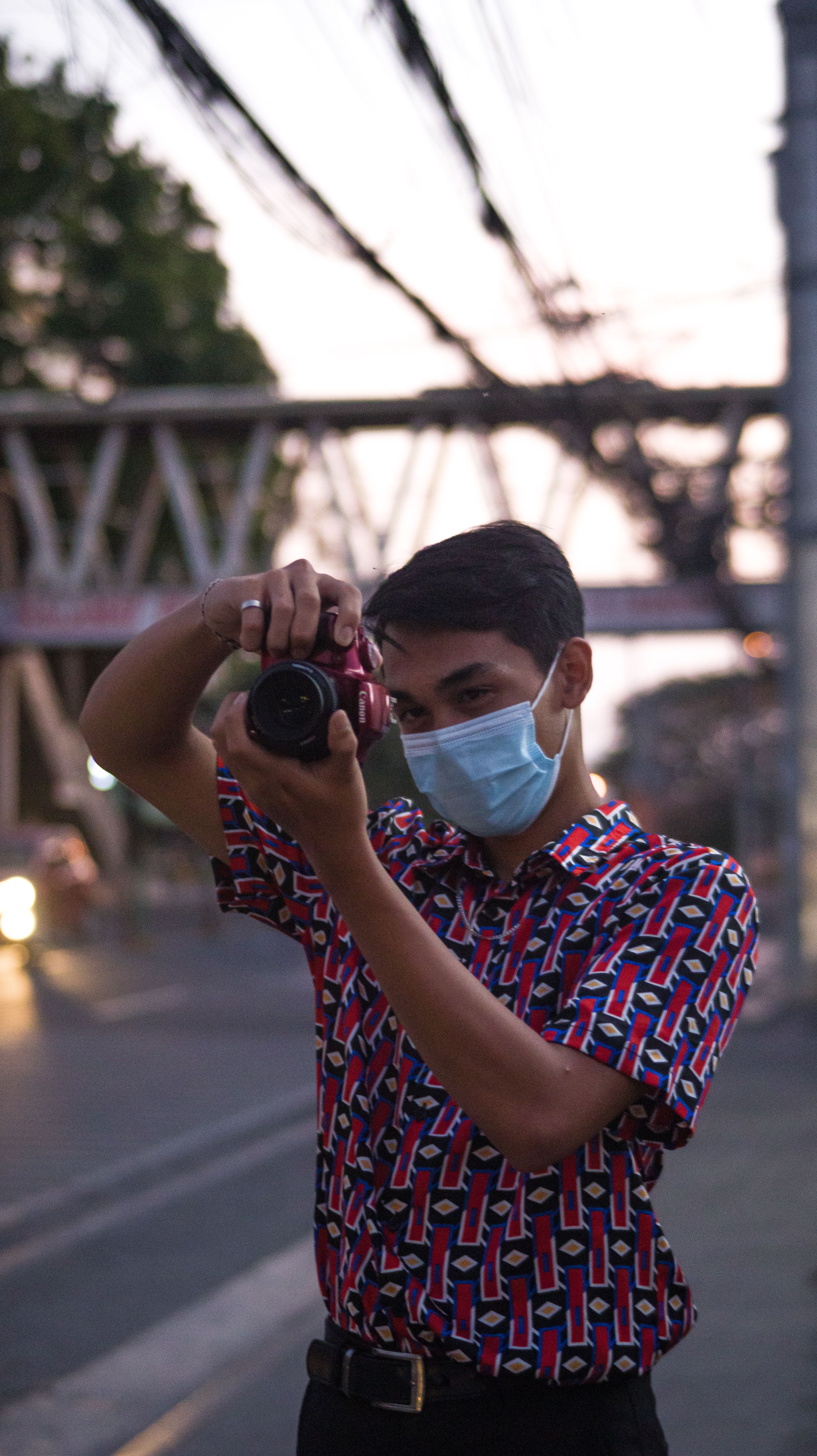 A young photographer with a mask takes pictures in an urban setting at twilight.