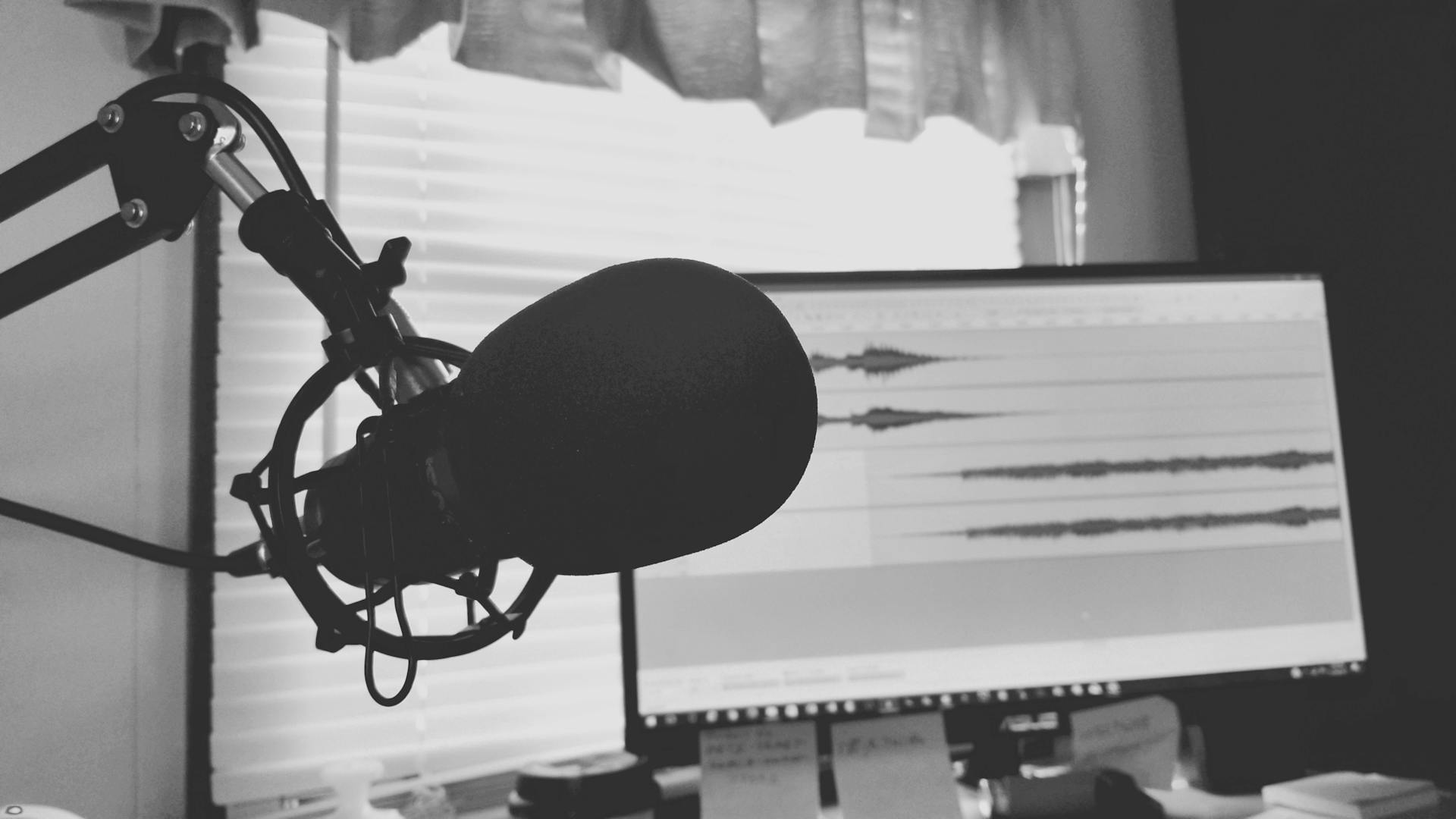 Black and white image of a podcast setup with microphone and waveform screen.