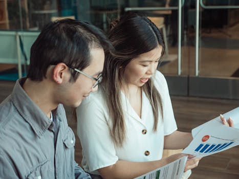 Two colleagues review documents during a business meeting in a modern office setting.