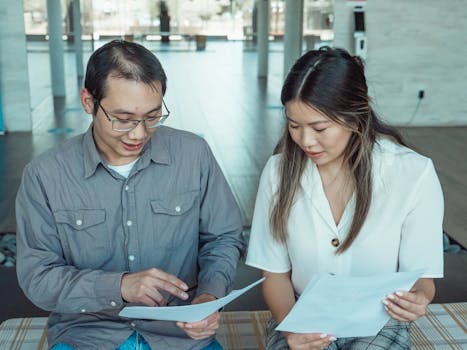 Two coworkers reviewing documents in a modern office, focused on teamwork and planning.