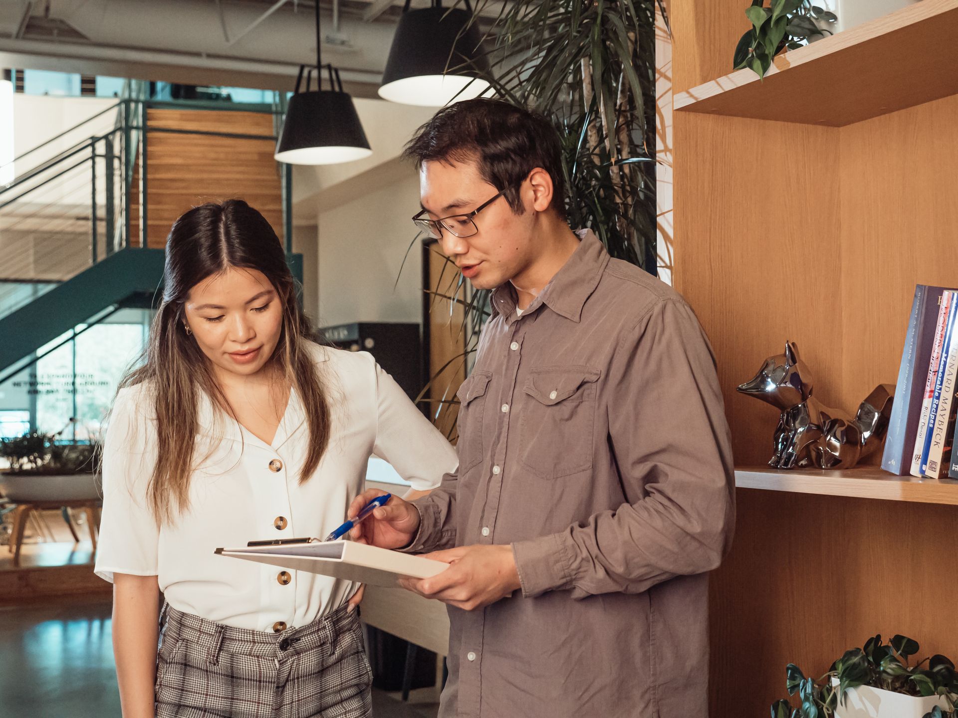 Two colleagues engage in a discussion while reviewing documents in a contemporary office setting.