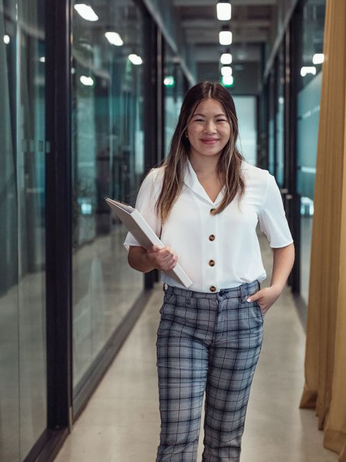 Free Smiling woman holding documents confidently walking in modern office corridor. Stock Photo