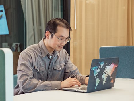 A man working on a laptop with a world map design in a contemporary office.