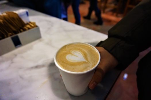 A hand holds a cup of coffee with elegant latte art on a marble countertop in a cozy cafe.