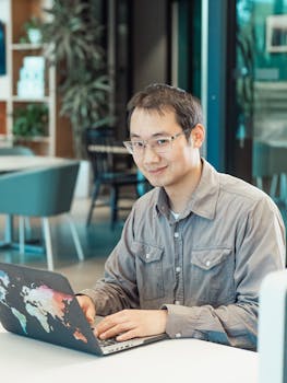 A young man working on a laptop in a modern office setting, casual and focused.
