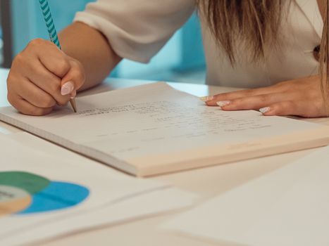 Hand writing on a notepad in an office. Close-up view with additional documents on desk.