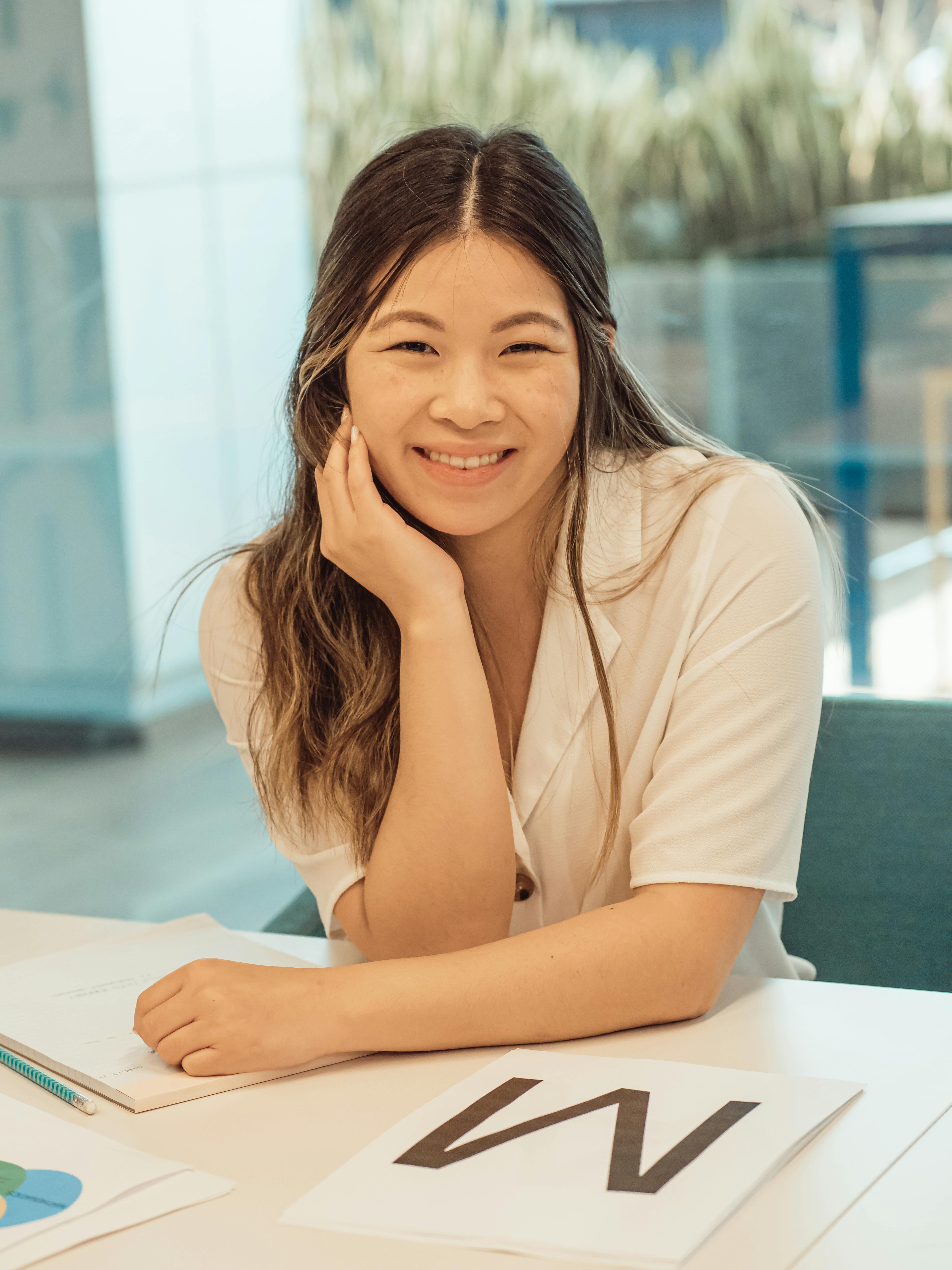 Happy woman in casual attire sitting at a desk indoors, exuding positivity.