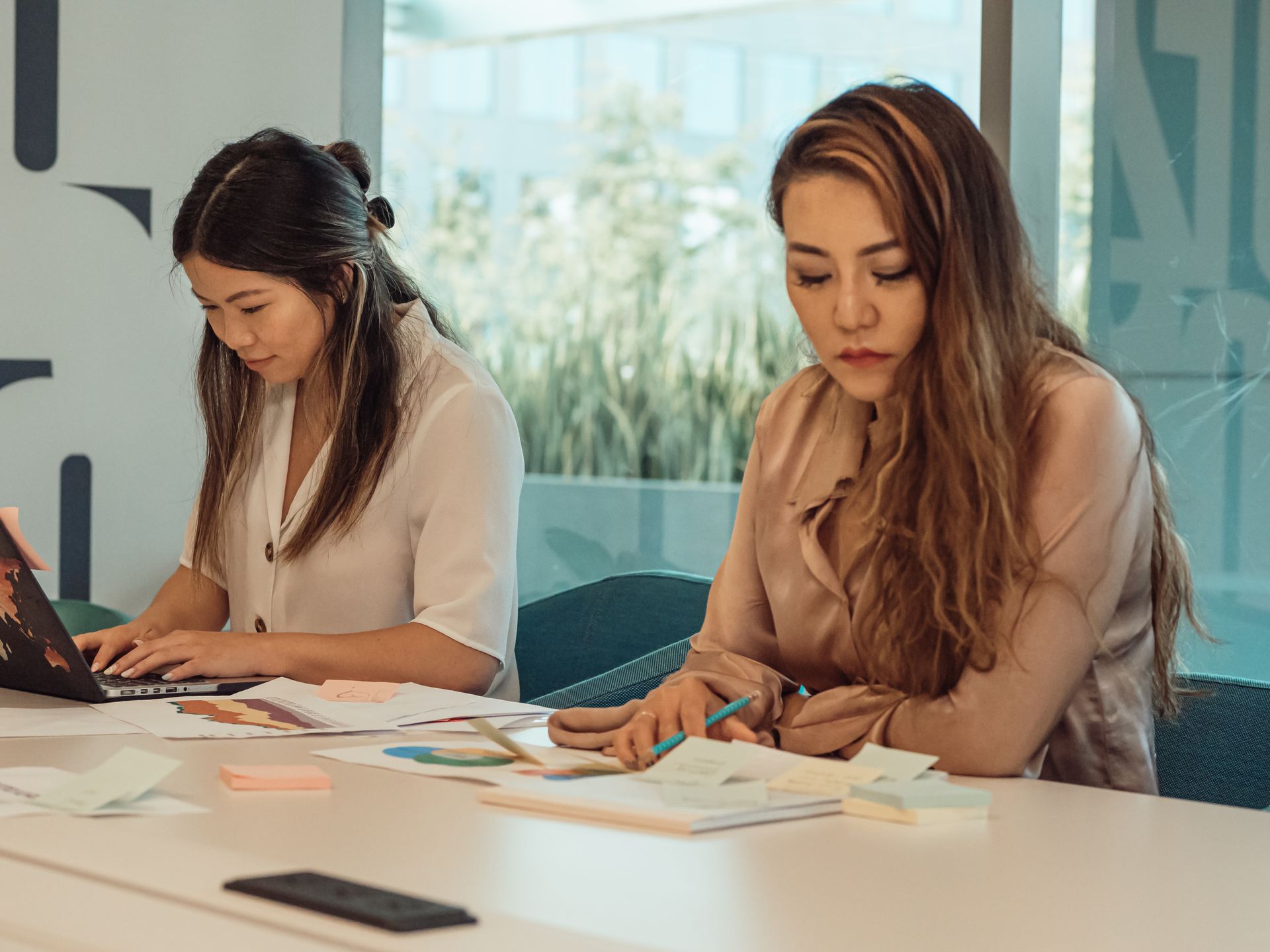 Focused women in modern office setting working on documents and laptop.