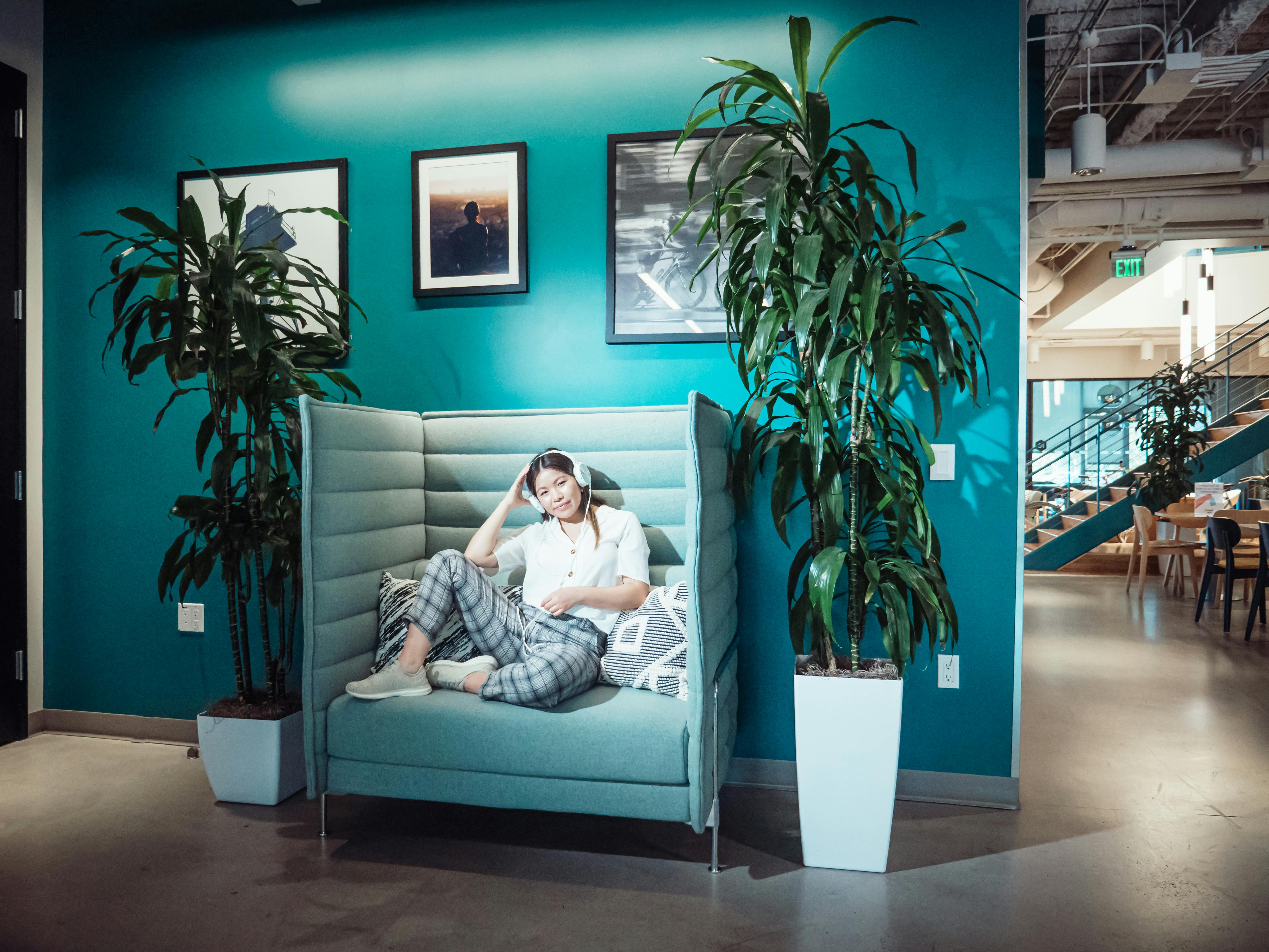 A woman relaxing on a sofa with headphones in a stylish, modern office. Bright and inviting workspace.