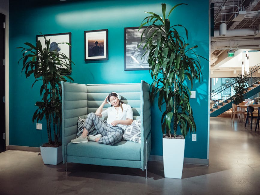 SoFi vs Marcus: Emergency Fund Strategy Explained A woman relaxing on a sofa with headphones in a stylish, modern office. Bright and inviting workspace.