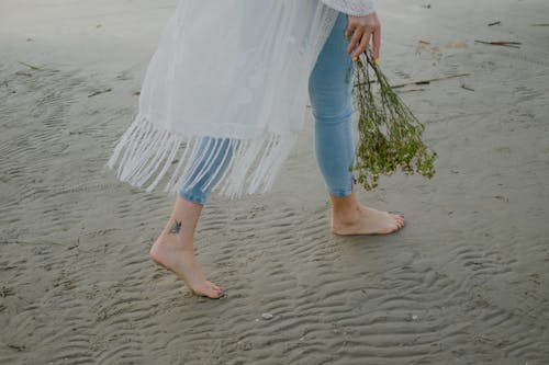 Free Person Standing Barefoot on Beach while Holding Flowers Stock Photo