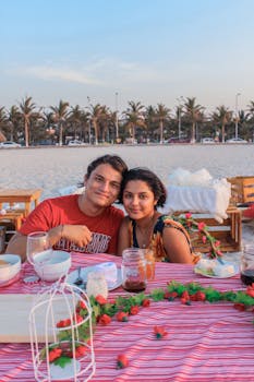 A couple enjoying a romantic dinner by the beach at sunset.