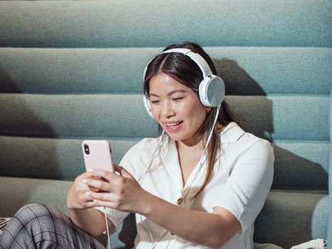 Young woman enjoying music with headphones and smartphone indoors on a comfortable seat.