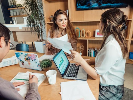 A group of young professionals collaborating around laptops and documents in a modern office.