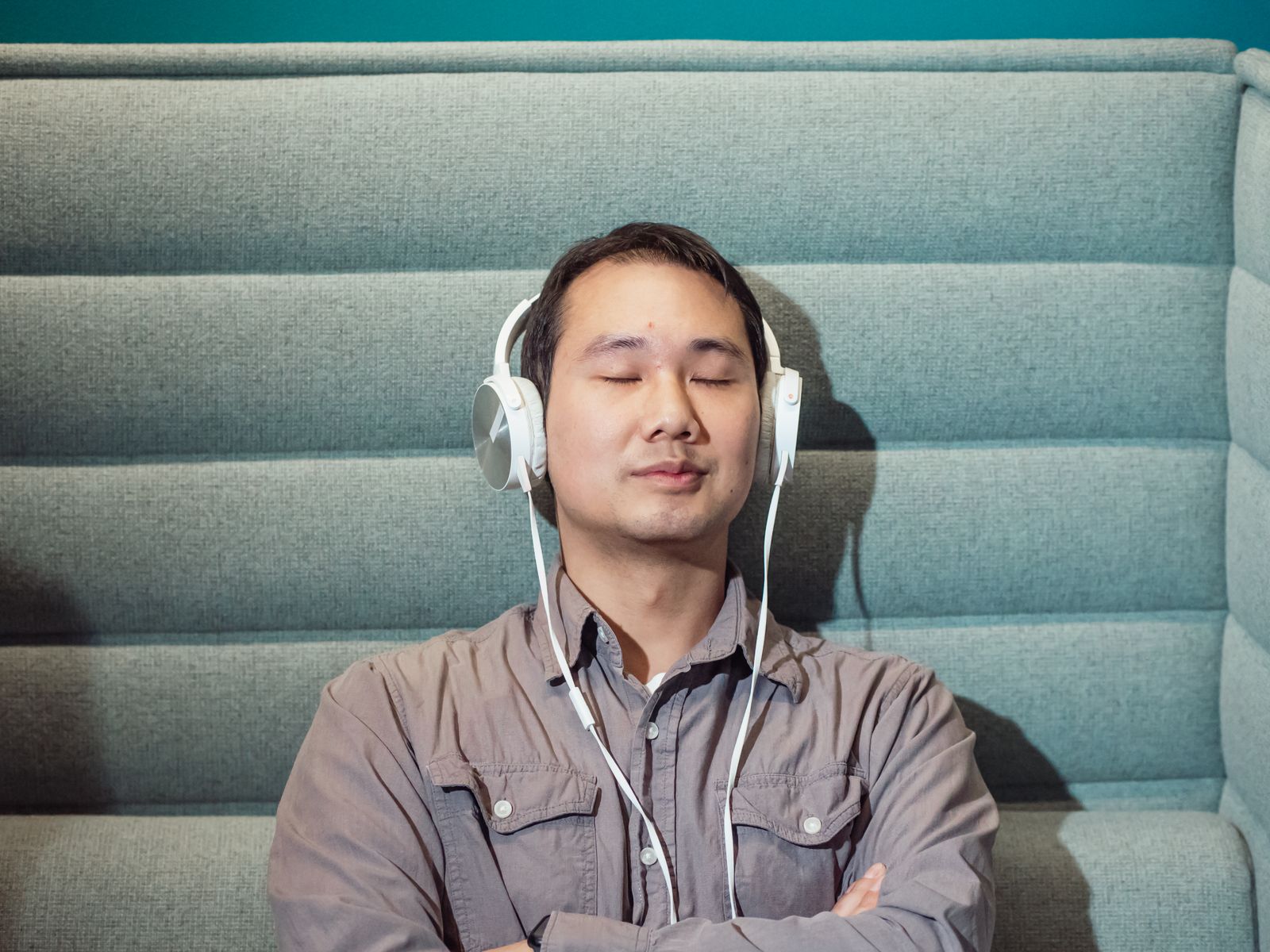 A man sitting indoors with his eyes closed, listening through over-ear headphones