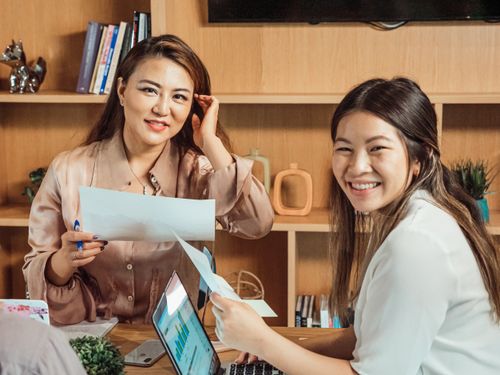 Free Two young women brainstorming and collaborating in a modern office setting, smiling and engaged. Stock Photo