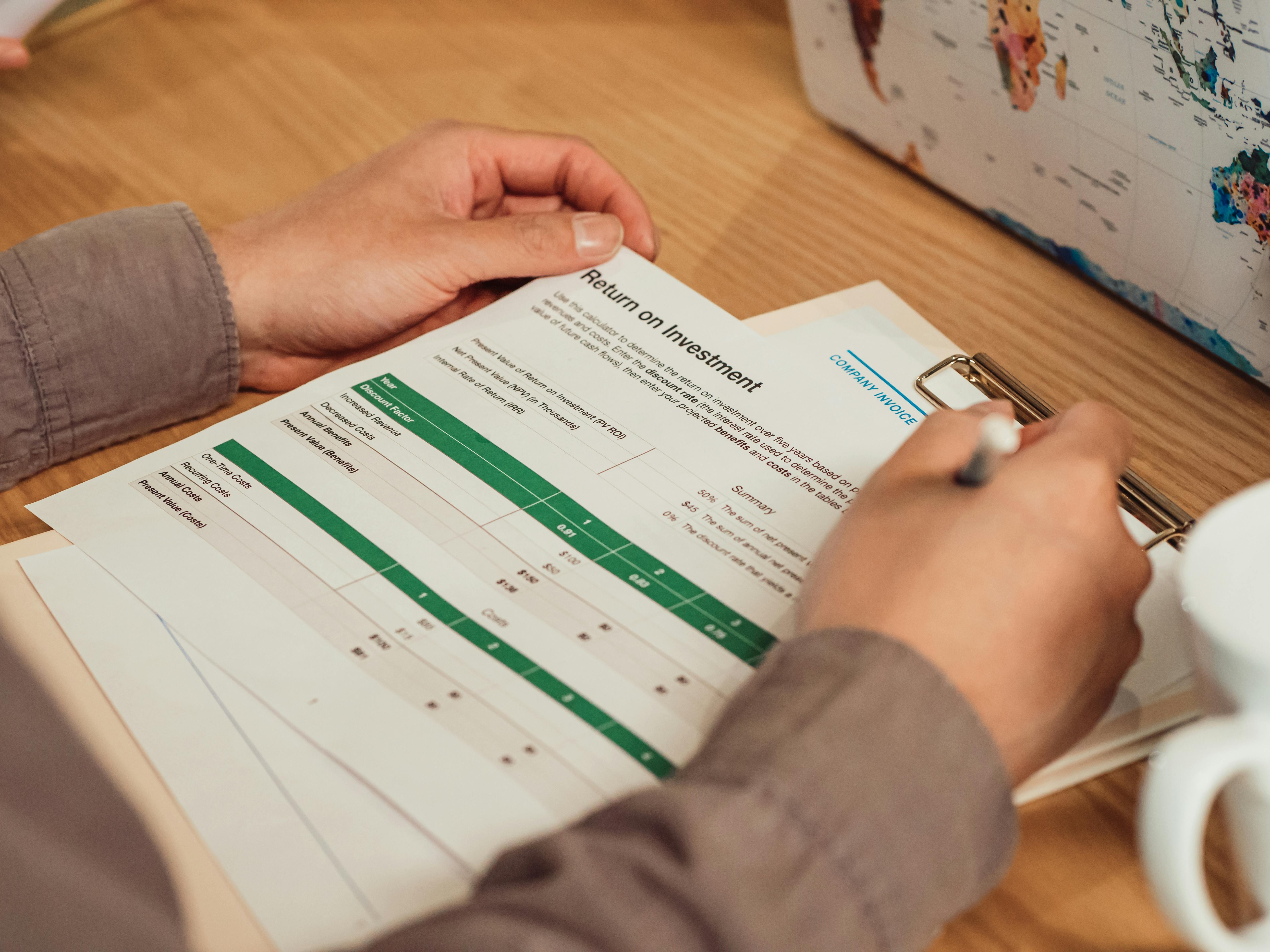 A person analyzing a return on investment report with a pen in hand on a desk.