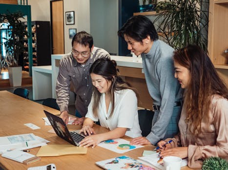 Diverse group of colleagues collaborating over a laptop in a creative office space.