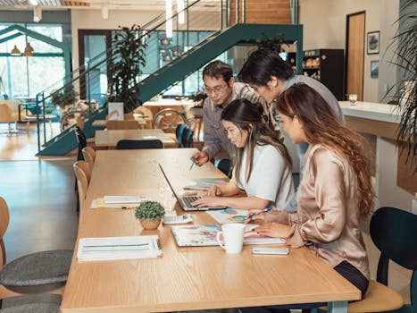 Four professionals collaborating in a modern workspace, focused on a project.