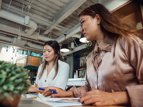 Two women collaborating at a desk in a modern office space, focusing on work tasks.