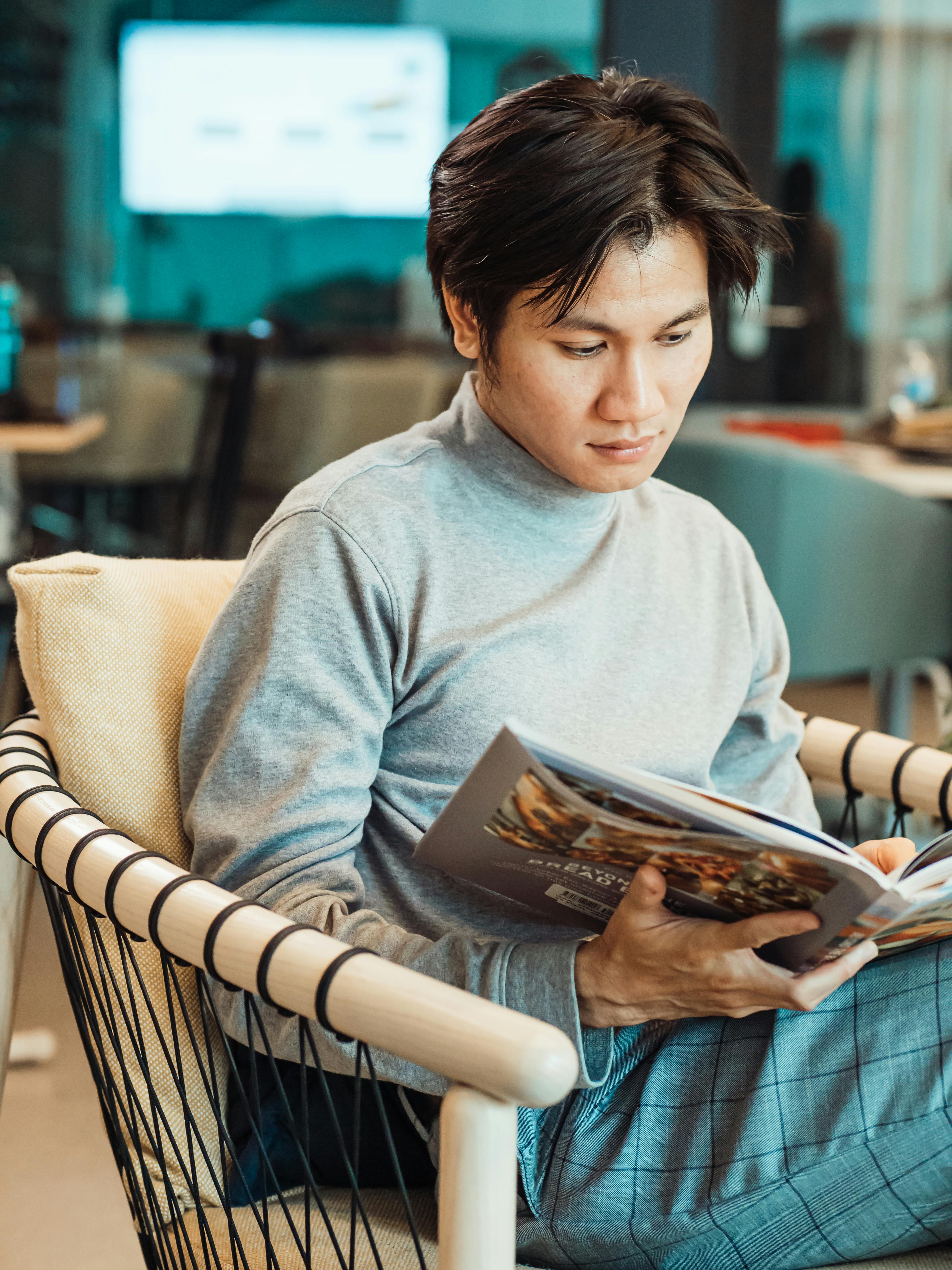 a man in gray turtleneck sweater reading while sitting on a chair