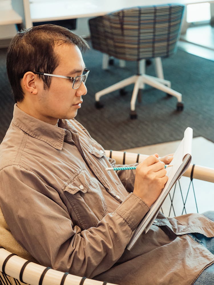 Man In Brown Long Sleeve Polo Shirt Sitting And Writing On A Pad Paper