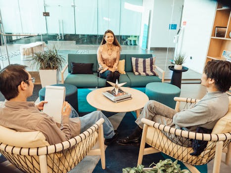 Three adults engaging in a casual meeting in a contemporary office lounge with modern furniture.