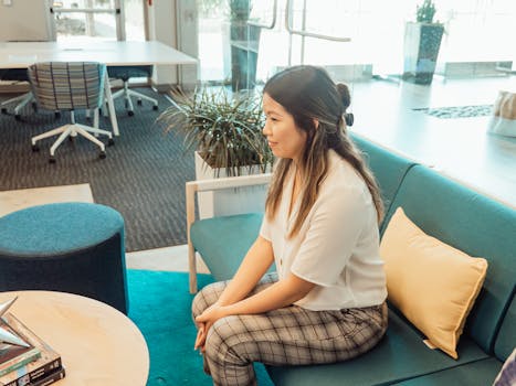 Asian woman in a modern office setting, sitting on a sofa for a meeting.