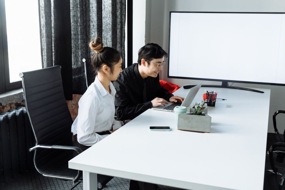 Asian man and woman working together on a laptop in a bright, modern office environment.