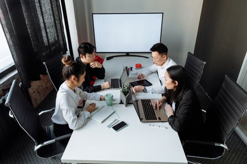 Free Four professionals collaborating over laptops in a bright, modern office space. Stock Photo