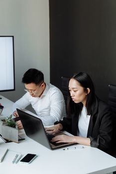 Two professionals focusing on their tasks in an office environment, using laptops.