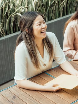 A young Asian woman laughing while holding documents at an outdoor meeting.