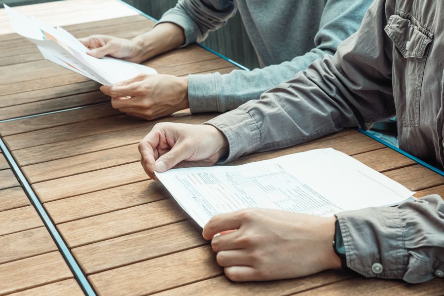 Two people reviewing business documents at an outdoor table, focused on paperwork.