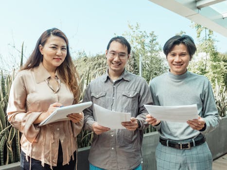 Three adults standing outdoors holding papers, smiling confidently.