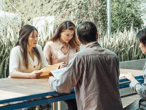 Free Four professionals engaged in a focused meeting outdoors, discussing documents. Stock Photo