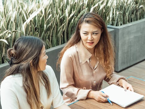 Two Asian women discussing business ideas in an outdoor office environment.