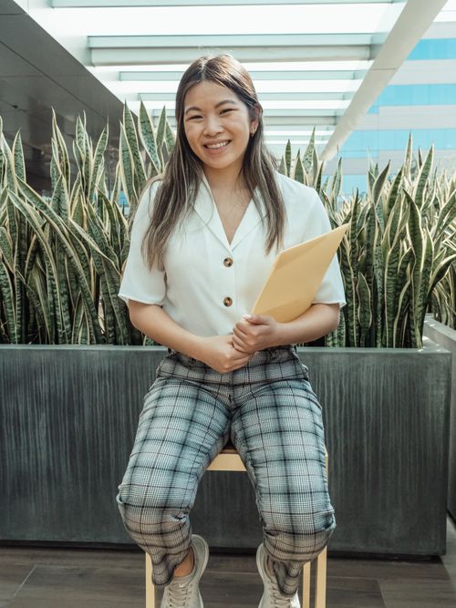 Free Cheerful Asian woman sitting indoors holding a folder, smiling. Stock Photo