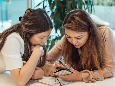 Two women collaborating in a modern office, reviewing information on a mobile device.