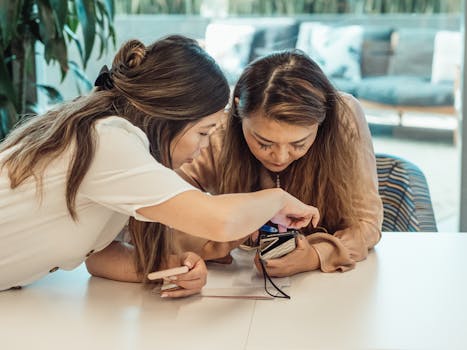 Two women in an office setting collaborating over a digital camera, embodying teamwork and technology.