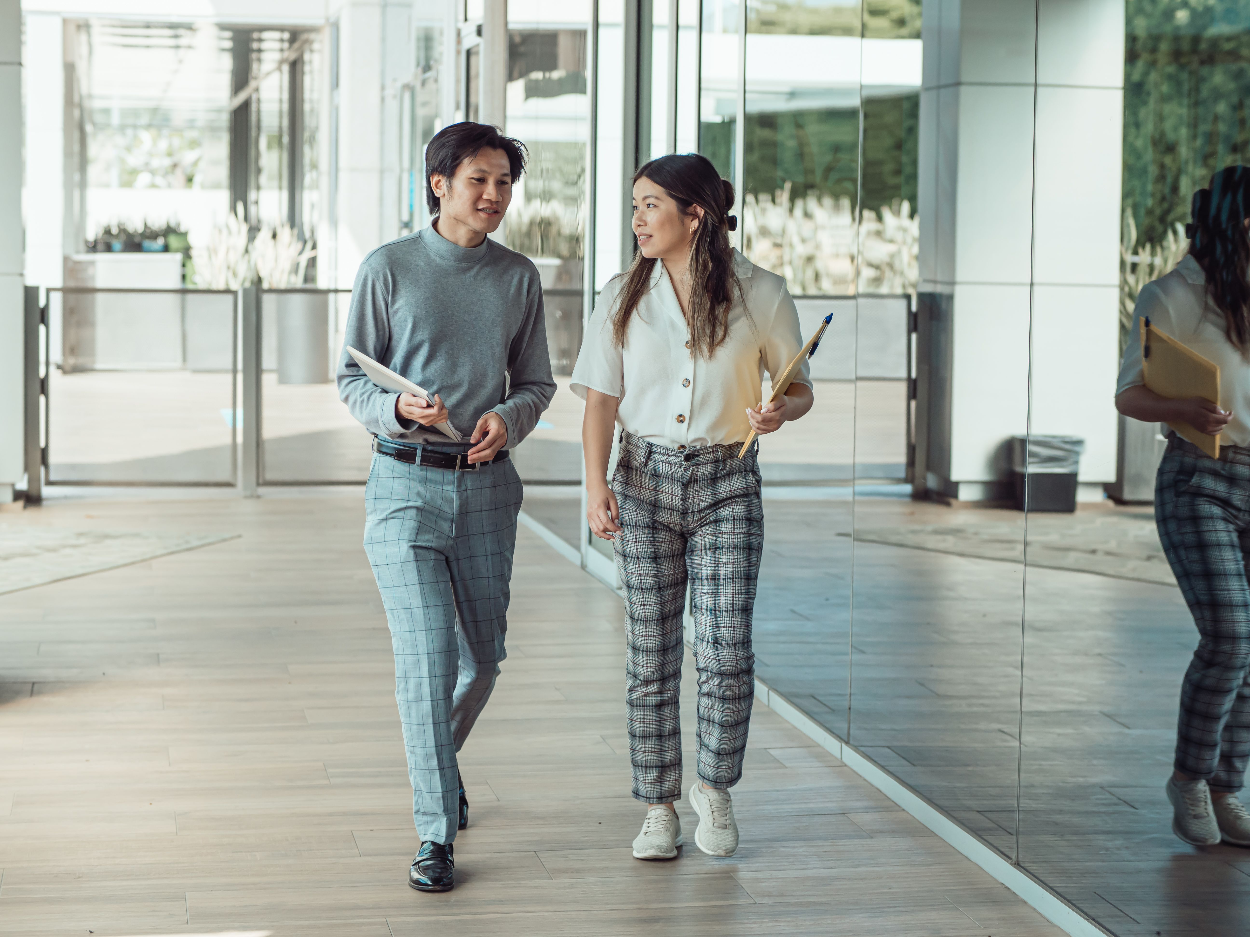 Two colleagues engaged in conversation while walking through a modern office hallway.