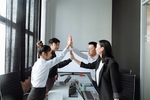 Four colleagues in a modern office high-fiving, celebrating teamwork and success.