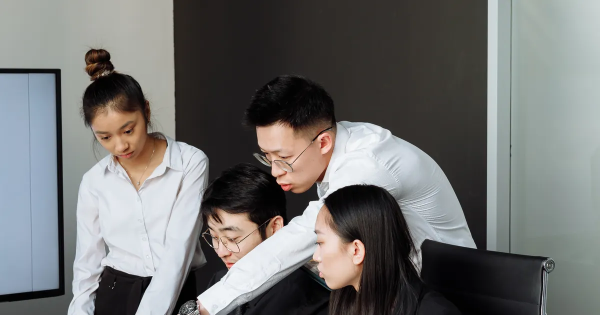 Four colleagues gathered around a laptop in an office, two of them bending over, representing OpenAI, Google, Anthropic Hold 84% of AI Agents. France Noticed