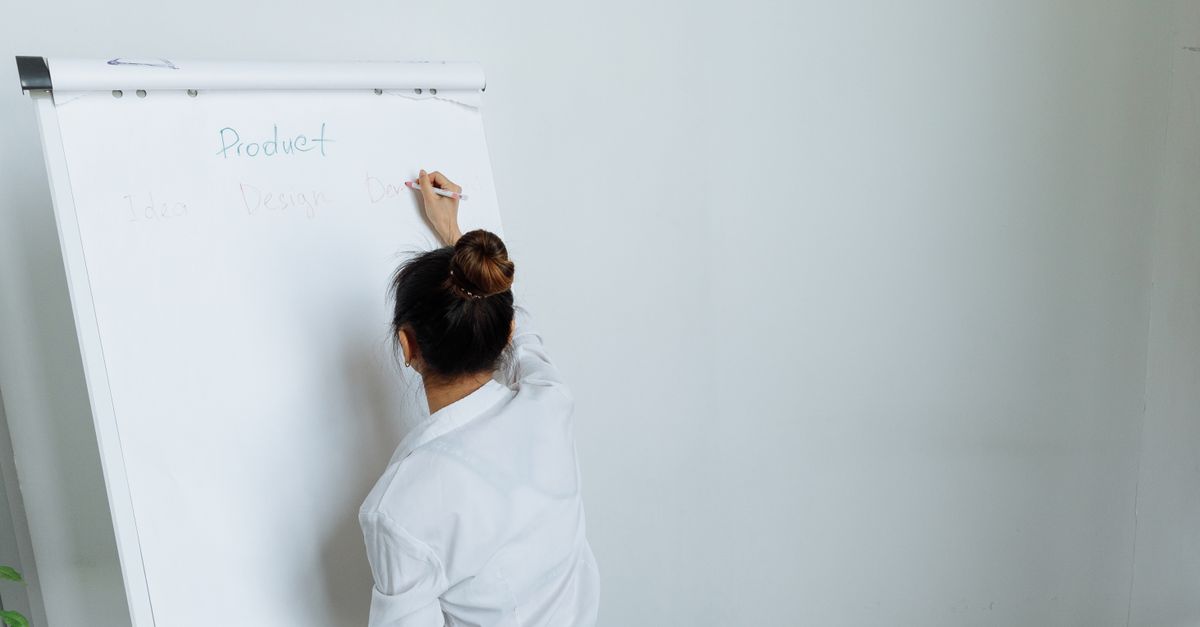 A woman in a white shirt writes on a flipchart during a presentation in an office.