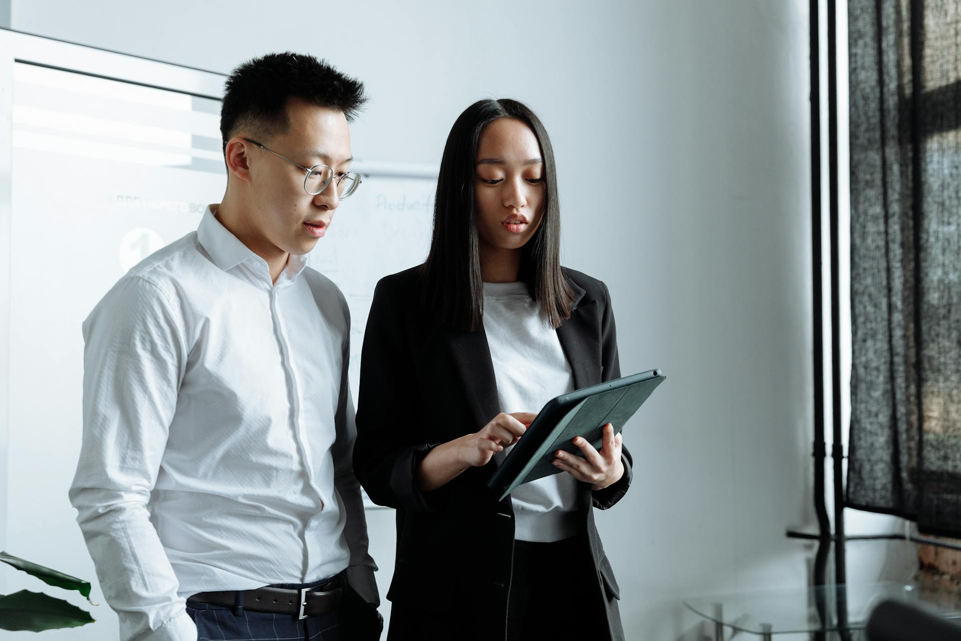 Two business people discussing work on a tablet in a modern office setting.