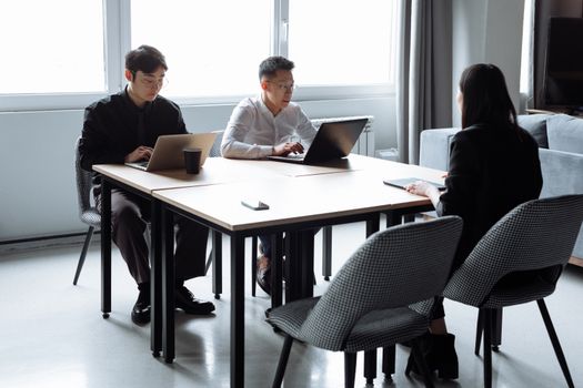 Three colleagues having a focused meeting with laptops in a modern office setting.